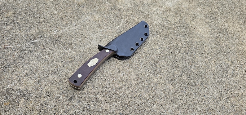 May include: A knife with a brown handle and a black leather sheath. The sheath has five stitching holes.