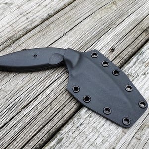 May include: A black knife with a black sheath. The sheath has multiple snap closures.
