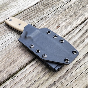 以下が含まれることがあります： 複数のスナップ留め具が付いた黒い革製のナイフシースと、タンのハンドルが付いたナイフが内側にあります。