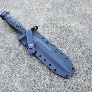 May include: A black knife sheath with a black knife inside. The sheath has a strap and multiple holes.