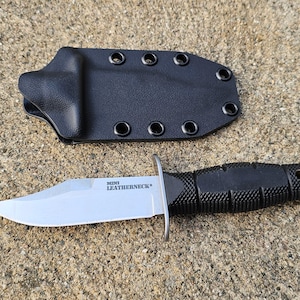 Könnte beinhalten: Ein schwarzes Messer mit silberner Klinge und schwarzem Griff, neben einer schwarzen Scheide. Auf der Klinge steht "MINI LEATHERNECK". Der Griff hat eine strukturierte Oberfläche.