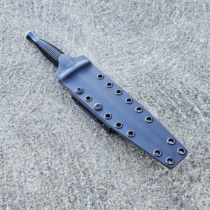 May include: A black leather knife sheath with multiple rows of snap buttons. The sheath is designed to hold a knife with a pointed tip.