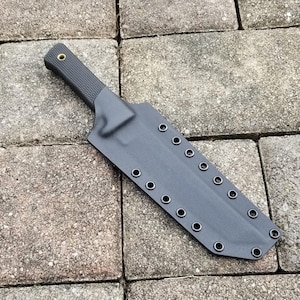 Puede incluir: Una funda de cuchillo negra con una fila de ojales a lo largo del lado. La funda está hecha de un material duradero y tiene un diseño simple.