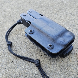 May include: A black multi-tool with a black sheath and a black lanyard. The multi-tool is partially open, revealing various tools. The sheath is secured with two black screws. The lanyard is knotted.
