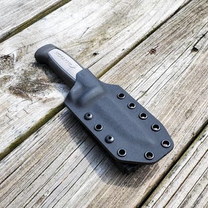 May include: A black leather knife sheath with a silver knife inside. The sheath has multiple rows of stitching around the edges.
