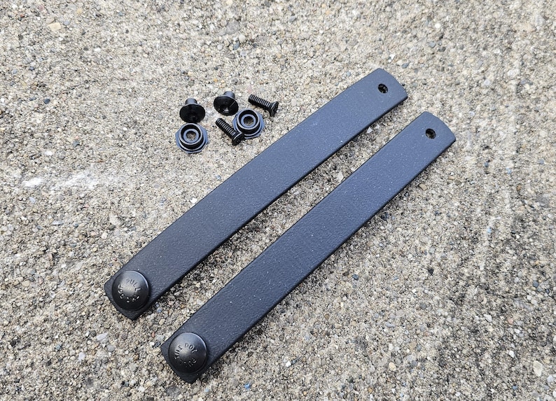 May include: Two black leather straps with metal snaps. The straps are approximately 30 cm long and 2.5 cm wide. The snaps are round and have a black finish.