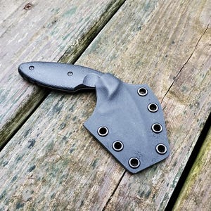 May include: Black knife with a black sheath. The sheath has multiple holes for attaching to a belt.