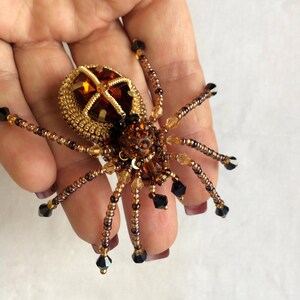 May include: A beaded spider brooch with a brown and gold body and black crystal accents.