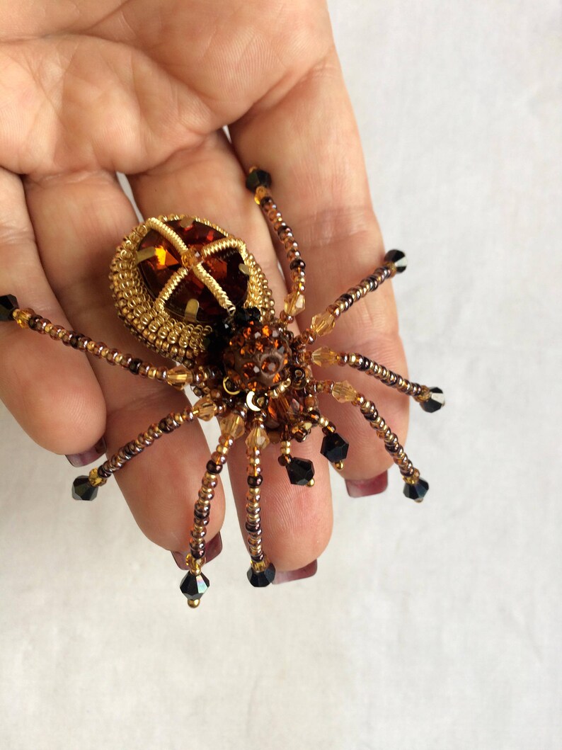 May include: A beaded spider brooch with a brown and gold body and black crystal accents.