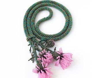 May include: A beaded necklace with a green iridescent cord and three pink flower accents.