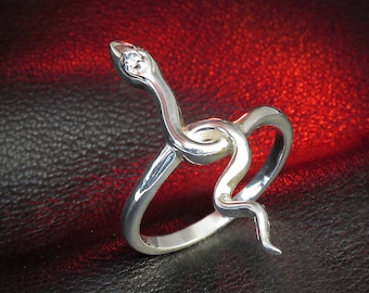 May include: A silver ring shaped like a snake with a small clear stone in its head.