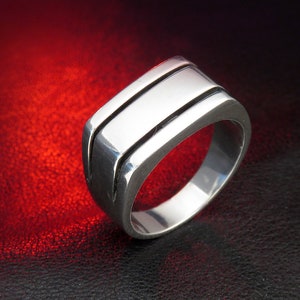 May include: A silver ring with a wide band and two parallel grooves running along the top.