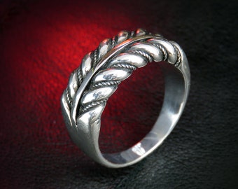 May include: A silver ring with a detailed leaf design. The ring features a central leaf shape with braided rope-like detailing on either side. The ring is set against a dark background with a red gradient.