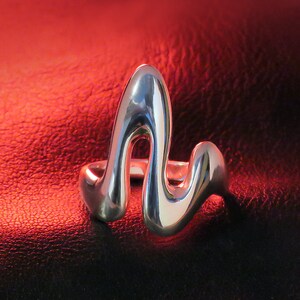 Peut inclure: Une bague en argent avec un design unique et abstrait. La bague est en métal lisse et poli et a une forme ondulée.