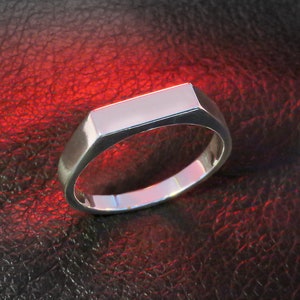 May include: A silver ring with a flat, rectangular top. The ring is on a red leather background.