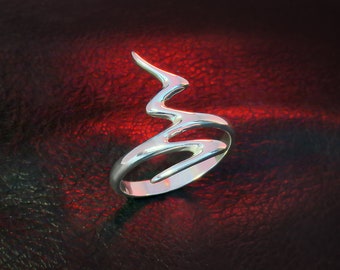 May include: A silver ring with a unique, abstract design that resembles a stylized flame or lightning bolt. The ring is shown on a red background.