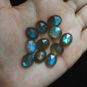 May include: A collection of oval-shaped labradorite gemstones with an iridescent blue and green sheen. The stones are faceted and have a smooth, polished finish.