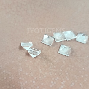 May include: A group of eight clear glass pyramid-shaped crystals on a brown textured surface. The crystals are all the same size and shape, and they are arranged in a random pattern.