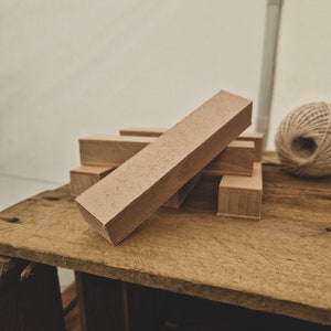May include: A stack of light brown wooden blocks, with one block lying on top of the others. The blocks are on a wooden surface.