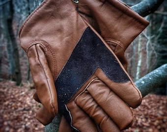 May include: A pair of brown leather gloves with black accents. The gloves are hanging from a branch.