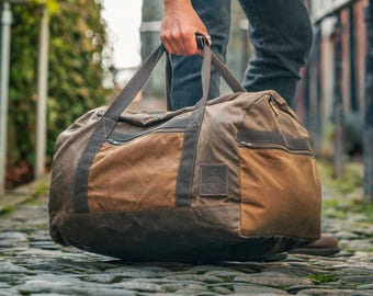 May include: A brown and tan duffel bag with a rectangular leather patch and zipper pockets. The bag has two handles and a shoulder strap. The bag is made of a waxed canvas material.