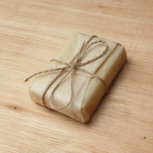May include: A small rectangular package wrapped in brown paper and tied with twine. The package is sitting on a wooden surface.