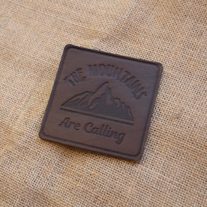 May include: A brown leather patch with the text "The Mountains Are Calling" and a mountain silhouette.