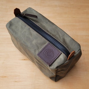 May include: A green canvas zippered wash bag with a brown leather patch that says "JOURNEYMAN HANDMADE" with a compass design.