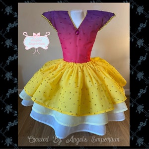 Può includere: Una gonna di tulle a strati gialla e bianca con un corpetto a gradiente di rosa e viola. Il corpetto ha una scollatura a V ed è decorato con strass. Anche la gonna è decorata con strass. L'abito è etichettato "Created By Angels Emporium".