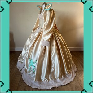 Puede incluir: Un vestido de bola de sat&eacute;n dorado con una aplicaci&oacute;n de rana verde y un ribete de piel blanca. El vestido tiene un corpi&ntilde;o ajustado y una falda completa.