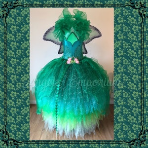 Puede incluir: Un disfraz de hada de tul verde y azul con un corpiño verde, purpurina y un diseño de alas de mariposa. El disfraz incluye una varita con detalles verdes y blancos.