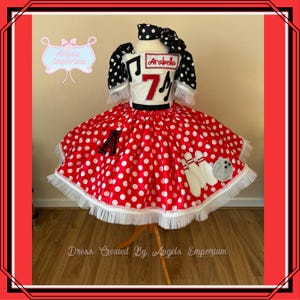 Op de afbeelding: Een rood-witte polkadotjurk met een wit lijfje met een zwart-wit bowlingpinontwerp en de naam "Arabella" en het nummer "7".