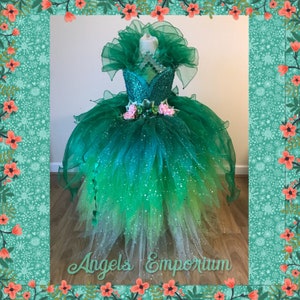 Puede incluir: Un vestido de tul verde y blanco con un corpiño de lentejuelas y un adorno de flores. El vestido tiene una falda de tul en capas con un degradado de verde a blanco. El vestido está en un maniquí y tiene un cuello de tul verde.