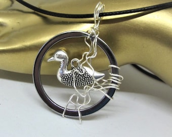 May include: A silver pendant necklace featuring a small silver duck charm inside a wire-wrapped circle. The necklace is on a black cord.