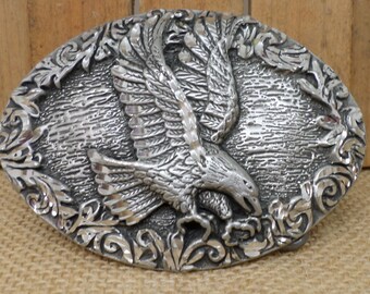 May include: Silver-toned belt buckle with an eagle in flight design. The eagle is detailed with feathers and has a floral design around it.