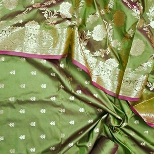 May include: Green silk fabric with a floral pattern. The fabric has a silver metallic thread woven into the design. The fabric is folded in half and the edges are visible.