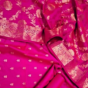 May include: A pink silk saree with a gold floral pattern. The saree has a border with a more intricate design.