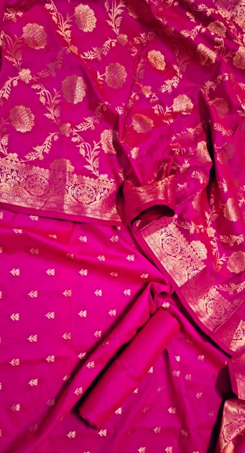 May include: A pink silk saree with a gold floral pattern. The saree has a border with a more intricate design.