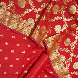 May include: Red fabric with a gold floral pattern. The fabric is folded in half and has a smaller piece of fabric with a smaller gold floral pattern on top.
