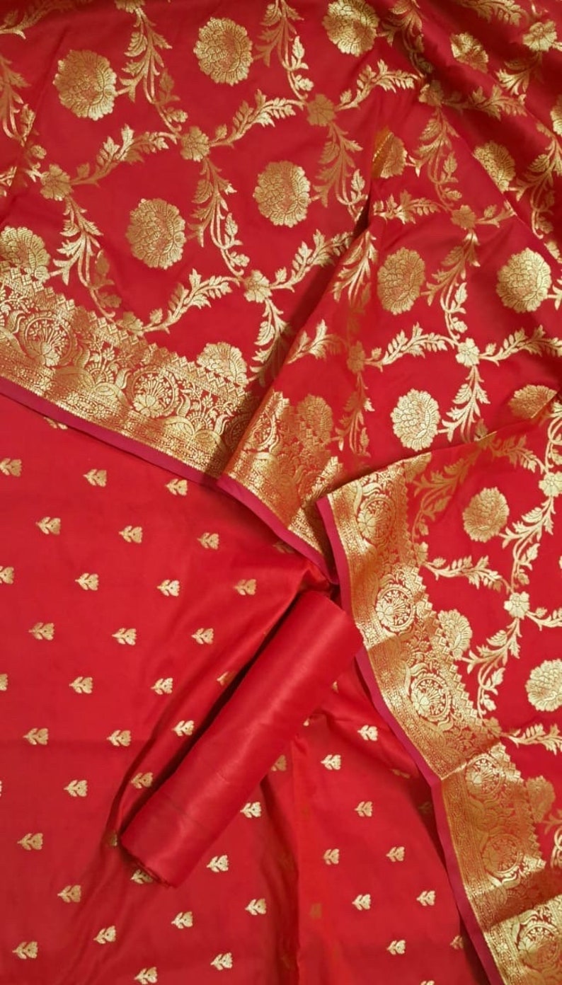 May include: Red fabric with a gold floral pattern. The fabric is folded in half and has a smaller piece of fabric with a smaller gold floral pattern on top.