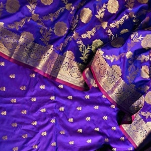 May include: Purple silk fabric with a gold floral pattern. The fabric is folded in half, and the bottom half has a smaller, more subtle gold pattern.