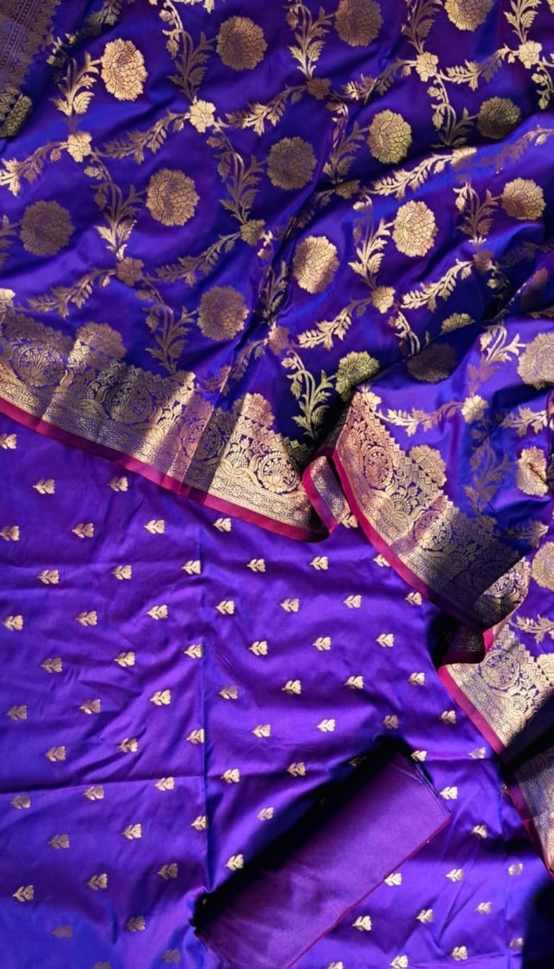 May include: Purple silk fabric with a gold floral pattern. The fabric is folded in half, and the bottom half has a smaller, more subtle gold pattern.