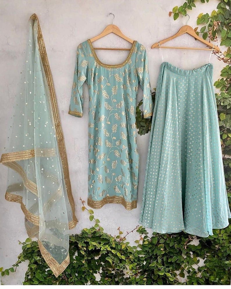 Peut inclure: Un ensemble trois pi&egrave;ces bleu clair compos&eacute; d'une tunique &agrave; manches longues avec une encolure d&eacute;gag&eacute;e, d'une jupe &eacute;vas&eacute;e et d'un dupatta transparent. La tunique et la jupe pr&eacute;sentent un motif floral dor&eacute;, tandis que le dupatta a une bordure dor&eacute;e.