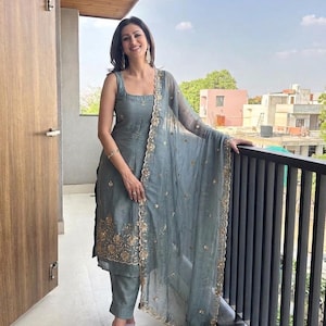 May include: A slate grey sleeveless kurta set featuring a square neckline and straight-leg trousers. The garment is adorned with intricate gold floral embroidery along the hem and a matching sheer dupatta with a scalloped gold embroidered border.