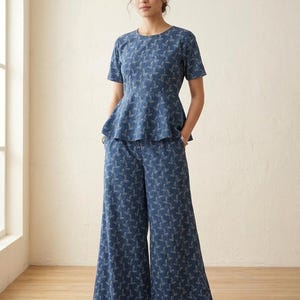 May include: A two-piece set consisting of a short-sleeved peplum top and wide-leg trousers. Both garments are made from a dark blue fabric featuring a repeating white botanical leaf pattern. The top has a round neckline and a flared waist detail.