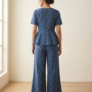 May include: A blue two-piece set featuring a short-sleeved peplum top and wide-leg trousers, both decorated with a delicate white botanical leaf pattern. The top has a round neckline and a visible vertical zipper closure along the upper back.