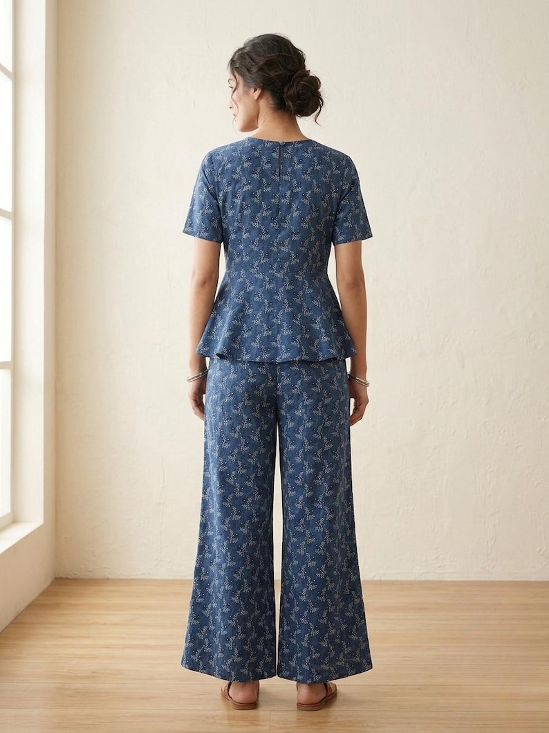 May include: A blue two-piece set featuring a short-sleeved peplum top and wide-leg trousers, both decorated with a delicate white botanical leaf pattern. The top has a round neckline and a visible vertical zipper closure along the upper back.