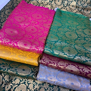 May include: A collection of folded fabric pieces featuring a repeating floral and leaf pattern in metallic gold thread. The fabrics are available in vibrant colors including hot pink, mustard yellow, dark green, deep maroon, and light lavender.