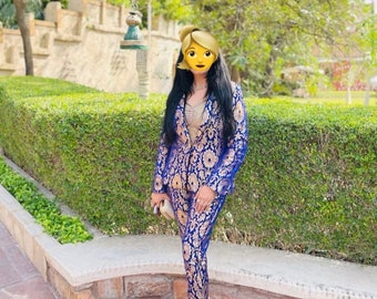 May include: A woman wearing a blue and gold patterned pantsuit. The suit has a floral design and is accessorized with a gold clutch and gold heels.