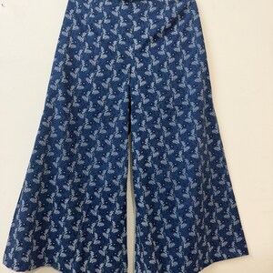 May include: Wide-leg trousers in a deep blue color featuring a repeating white botanical pattern of small leaves and tiny flowers. The pants have a high waistband and a loose, flowing silhouette that flares out from the hips to the hemline.